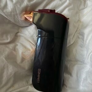 Luminess makeup airbrush with hand full of makeup tubes.